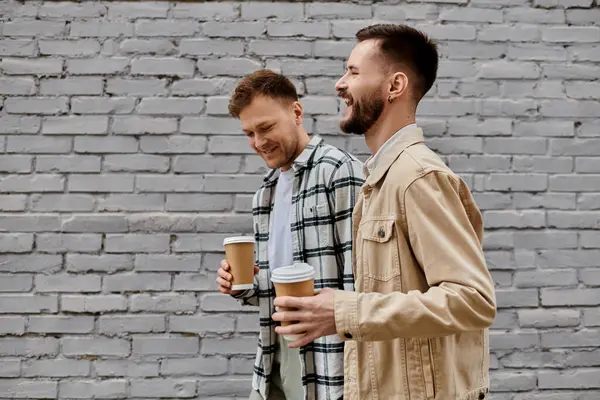 A happy gay couple in cozy attire enjoying freshly brewed coffee outdoors. — Stock Photo