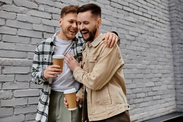 Two men in casual attire, standing together and enjoying a cup of coffee outdoors. — Stock Photo
