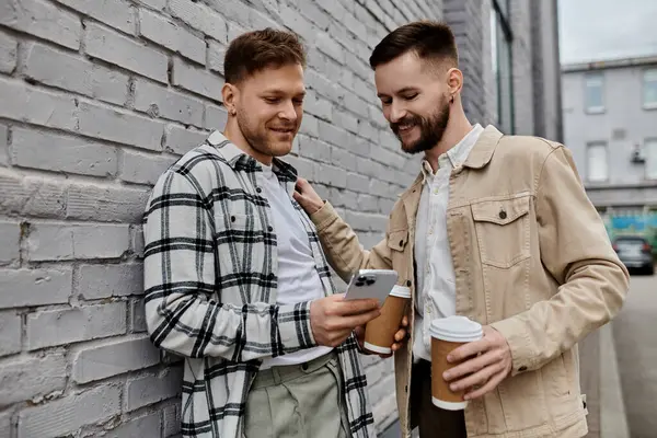 Un couple gay heureux en tenue confortable se tient à côté d'un mur de briques à l'extérieur. — Photo de stock