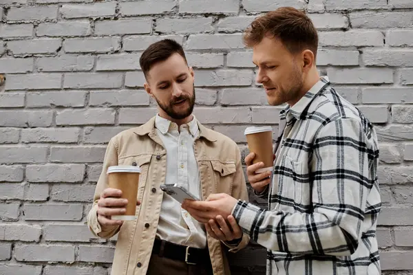 Two content men in casual attire, standing side by side, holding coffee cups outdoors. — Stock Photo