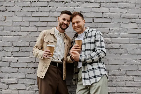 Happy gay couple in casual attire enjoying drinks outdoors. — Stock Photo