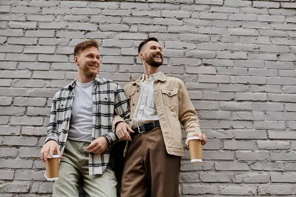 Dois homens de roupas casuais estão perto de uma parede de tijolo, desfrutando uns dos outros companhia. — Fotografia de Stock