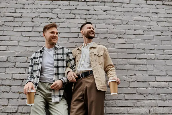 Two men in casual clothes stand by a brick wall, enjoying each others company. — Stock Photo