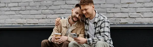 Couple in casual wear sits on bench, engrossed in cell phone. — Stock Photo