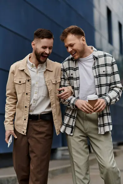 Dos hombres con atuendos casuales están uno al lado del otro en una acera soleada de la ciudad. - foto de stock