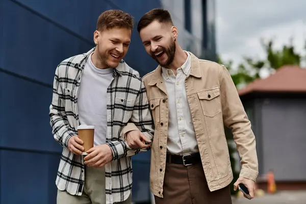 Two men in casual attire delightfully holding beverages. — Stock Photo