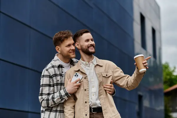 Due uomini in abbigliamento casual, tenendo tazze di caffè all'aperto. — Foto stock