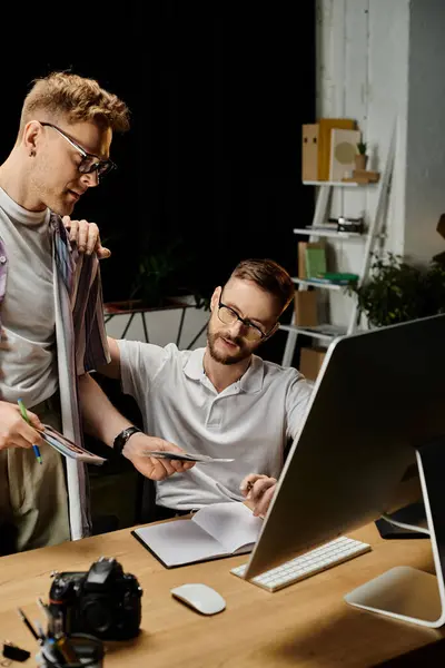 Two men in casual attire sit at a desk, engrossed in the laptop screen. — Stock Photo