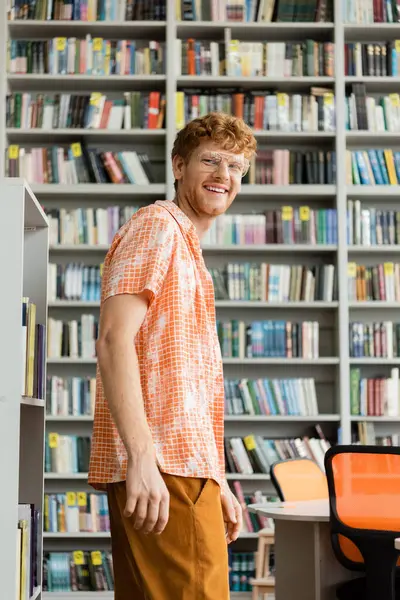 Ein junger Mann steht vor einem Bücherregal in einer Bibliothek, vertieft in das Lernen. — Stockfoto