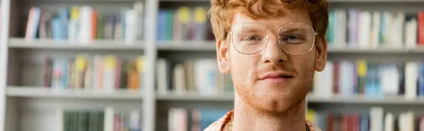 A scholarly man with glasses stands before a towering bookshelf. — Stock Photo