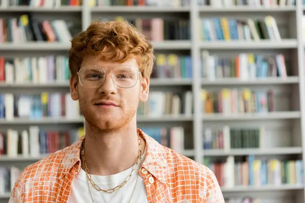 A young man with glasses browses books in a library. — Stock Photo