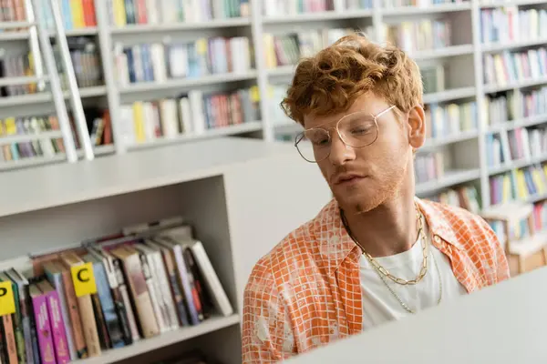 A man in glasses seated before a bookshelf. — Stock Photo