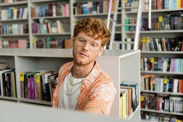 A man engrossed in study at a desk in front of a bookshelf. — Stock Photo