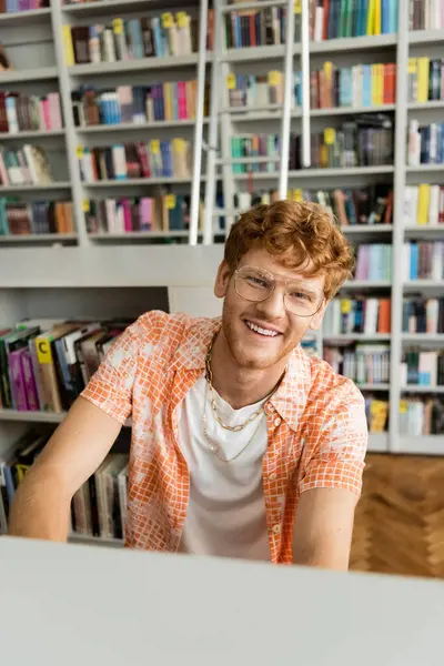 A man sits at a table in front of a bookshelf, immersed in studying and learning. — Stock Photo