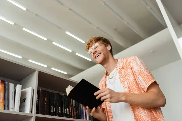 A man stands before a bookshelf, book in hand. — Stock Photo
