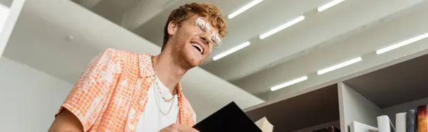 Ein Mann lacht, während er ein Buch in der Bibliothek hält. — Stockfoto