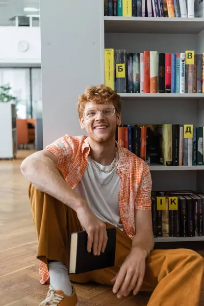 A man sits on the floor before a bookshelf. — Stock Photo