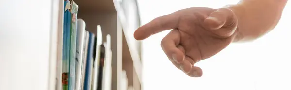 A hand reaches for a book in a bookcase. — Stock Photo