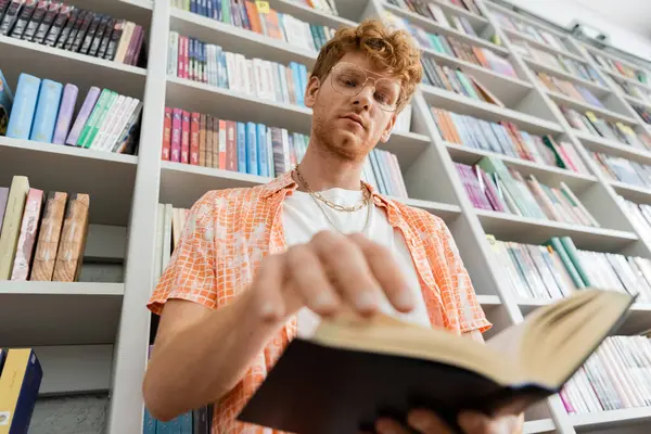 A man engrossed in a book amidst the shelves of a library. — Stock Photo