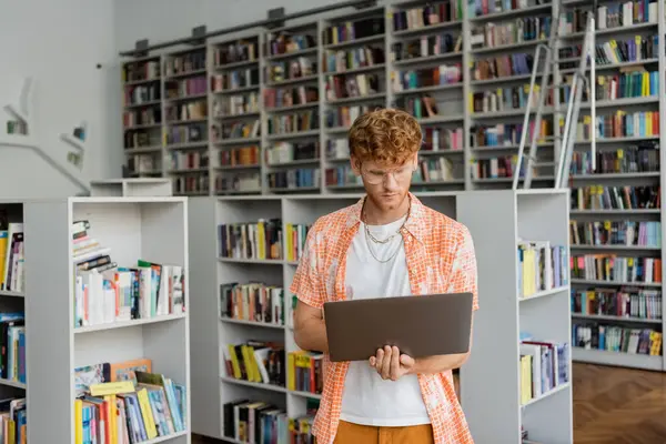 Man in front of books, holding laptop. — Stock Photo