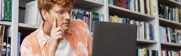 A young man immersed in study, focused on his laptop in a library. — Stock Photo