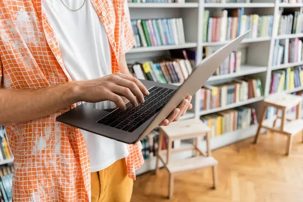 A young man engrossed in his laptop amidst rows of books in a library. — Stock Photo