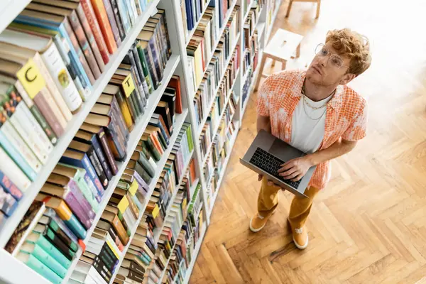A young man absorbed in using a laptop while studying in a library. — Stock Photo