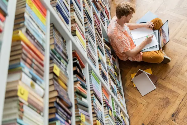 A man, young and handsome, sits on the floor before a bookshelf. — Stock Photo