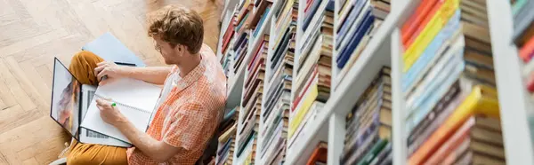 Ein Mann, tief konzentriert, schreibt in einer Bibliothek. — Stockfoto