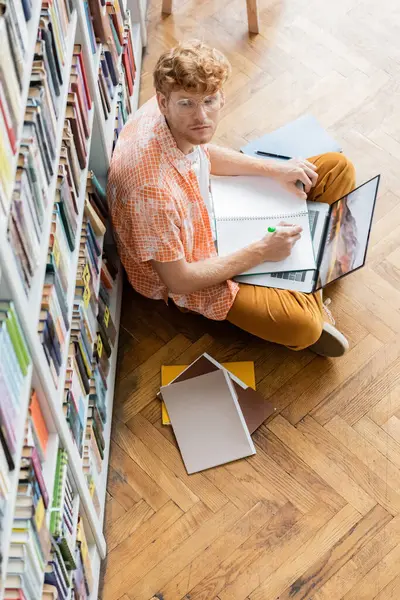 A young man seated before a library bookshelf. — Stock Photo