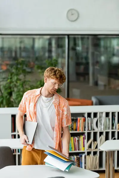 A young man standing before a table, holding a book. — Stock Photo