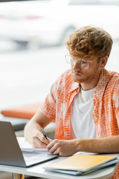 Un giovane uomo siede a un tavolo assorto nel suo computer portatile. — Foto stock