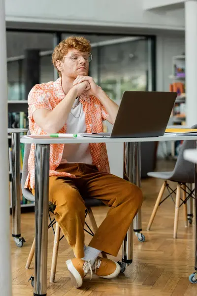 Un jeune homme concentré sur un ordinateur portable à une table. — Photo de stock
