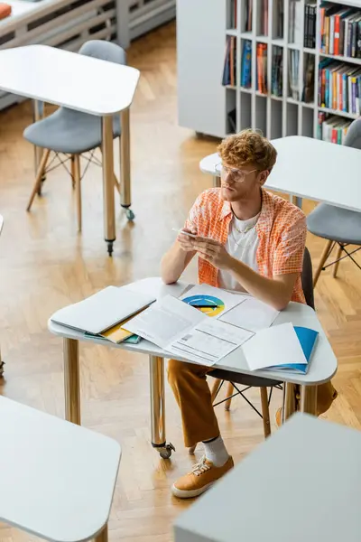 A young man sits at a table in a library, deep in study and contemplation. — Stock Photo