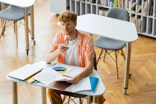 A person engrossed in a book and cell phone at a table. — Stock Photo