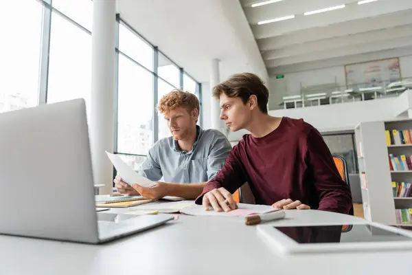 Due giovani uomini si concentrano sullo schermo del computer portatile, assorti nella sessione di studio a tavola. — Foto stock