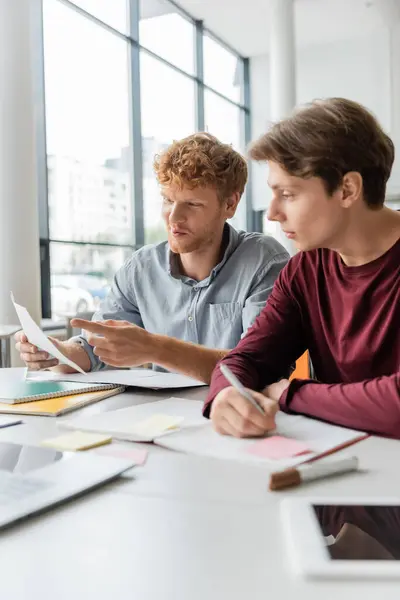 Two men deep in study, papers and pens scattered on the table. — Stock Photo