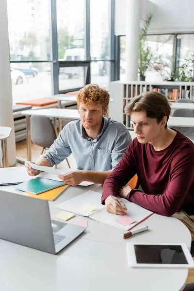 Zwei junge männliche Studenten lernen zusammen mit einem Laptop an einem Tisch. — Stockfoto