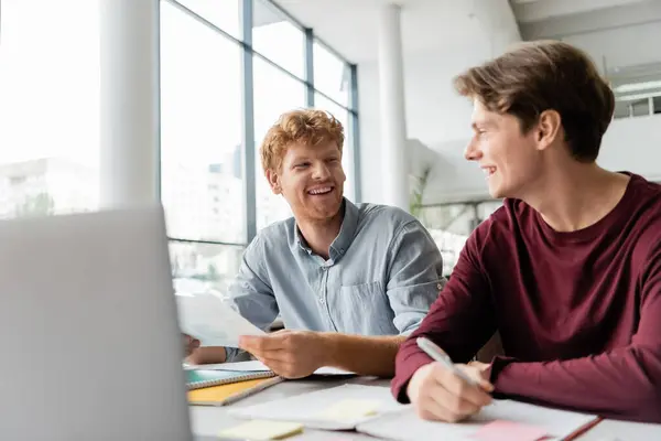Two young men sitting at a table, focused on studying together using a laptop. — Stock Photo