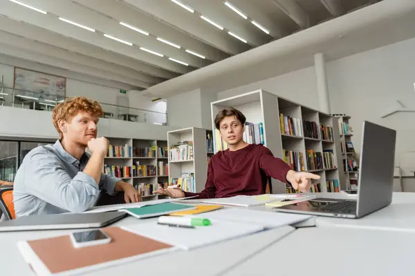 Due giovani studenti maschi si siedono a lavorare su un computer portatile a un tavolo. — Foto stock