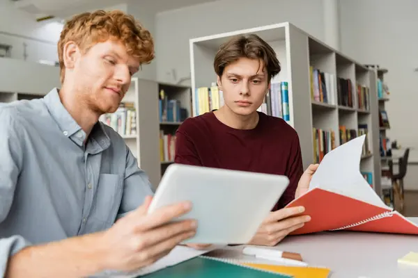 Two students engage with a tablet while seated at a table in a library. — Stock Photo