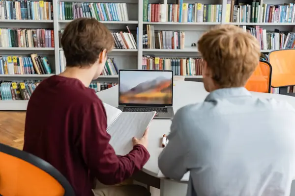 Two individuals engaged in a study session with a laptop on a table. — Stock Photo