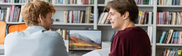 Two young male students are intensely studying together at a desk in front of a computer. — Stock Photo