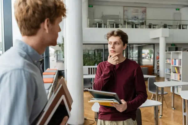 Due studenti di sesso maschile si impegnano in uno studio approfondito tra scaffali torreggianti di libri. — Foto stock
