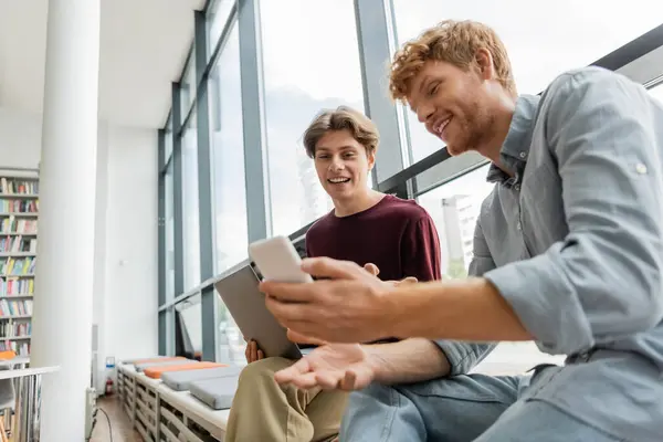Two male students engage with a tablet while seated on the floor. — Stock Photo