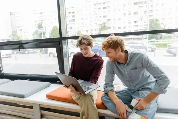 Two male students focused on a laptop while sitting on a bench. — Stock Photo