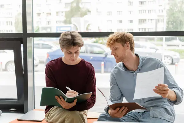 Two male students seated on a bench, engaged in studying papers together. — Stock Photo