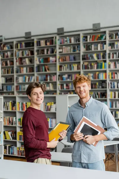 Two male students studying avidly in a library surrounded by countless books. — Stock Photo