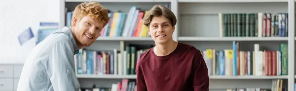 Two male students immersed in study, standing by a bookshelf. — Stock Photo