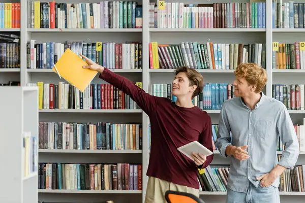 Two male students peruse a vast bookshelf in a scholarly setting. — Stock Photo